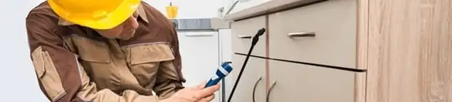 Roach exterminator applying treatment under kitchen cabinets in Buffalo, NY