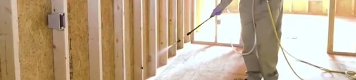Termite treatment technician applying spray along framing and unfinished walls in Buffalo, NY